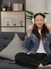 Obraz premium Young Asian Woman Dancing with Wireless Headphones on a Sofa