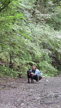 森の中で愛犬と触れ合いながら笑顔を見せる女性のアウトドアライフカメラ目線広角全身の縦動画