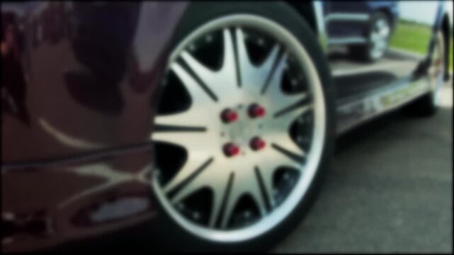 Detail shot of custom vehicle wheel, featuring modern aftermarket rim with intricate spoke pattern and bold red lug nuts, highlighting passion for car tuning and personalization