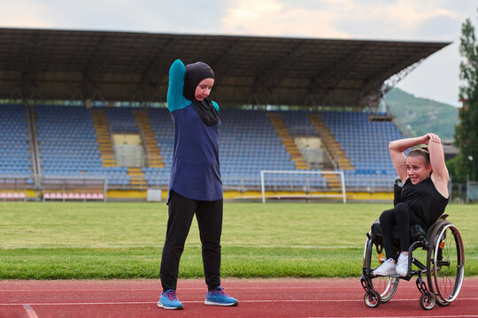 Wheelchair Athlete and Hijab-Wearing Runner Stretching Together on Outdoor Track in Stadium
