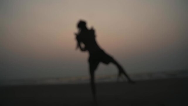 Blurred silhouette of a talented male artist skillfully spinning a rope dart during a captivating performance on the sandy shore, with the beautiful sunset creating a dramatic backdrop
