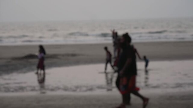 Anonymous and unrecognizable families walking and enjoying a serene evening on a wet sandy beach with calm ocean waves in the background, creating a peaceful and blurry holiday atmosphere