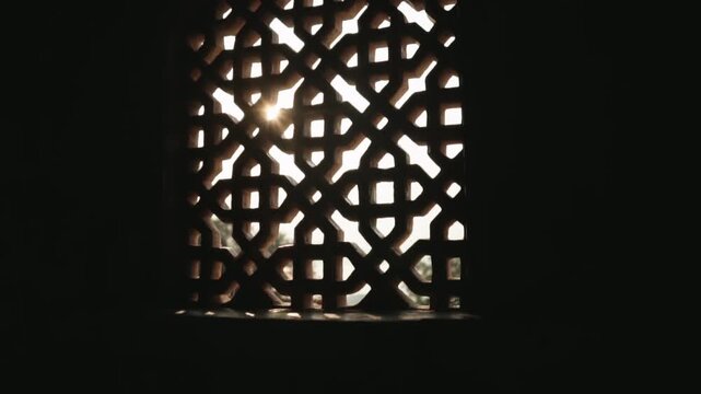 Bright sunlight streaming through a traditional jali, a stone lattice window with an intricate geometric pattern, illuminating the dark interior of a historic building with warm sunbeams