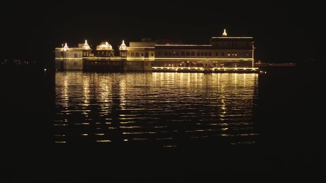 Famous Taj Lake Palace hotel floating on Lake Pichola in Udaipur, India, with golden lights reflecting on the calm water at night, showcasing its stunning traditional rajasthani architecture