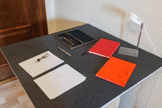 Desk with notebooks, drafting set, paper and lamp, high-angle side view with door in background