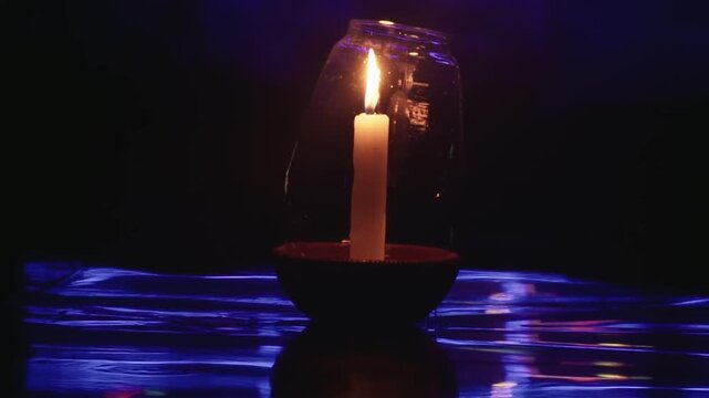 Mystical scene featuring a single burning candle inside a glass jar, casting a warm glow over a rippling blue surface in a dark, spiritual setting, creating a peaceful and contemplative mood