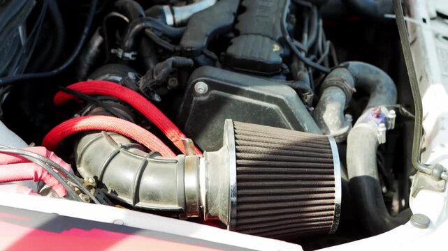 Detailed look at power of engine with performance air filter, intake system, and red braided lines visible. Image highlights complex network of mechanical components under hood of car.