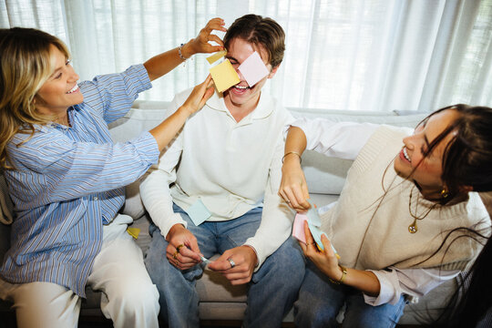 Friends enjoying a playful moment with sticky notes together on a cozy couch