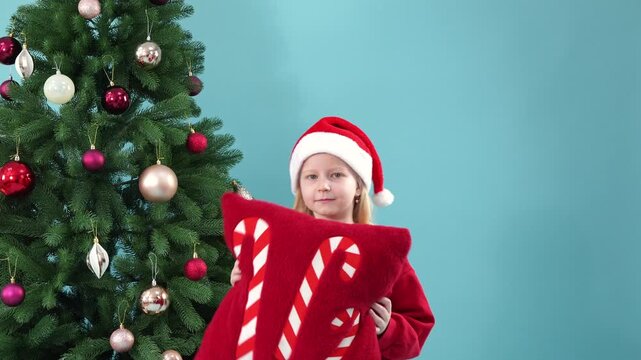 Happy little girl holding decorative christmas pillow near tree