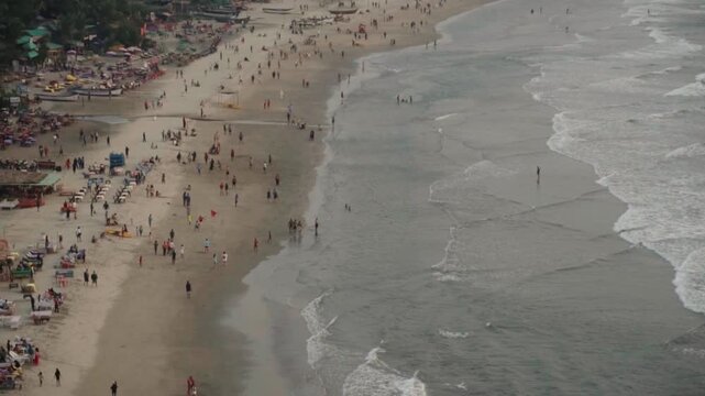 Aerial view of a crowded sandy beach with many tourists enjoying the ocean and relaxing on the shore during a summer vacation day at a popular seaside resort destination