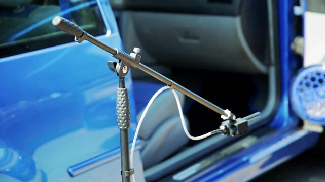 Precision microphone on stand capturing sound level readings from powerful audio system installed in customized blue car, prepared for judging at auto sound competition