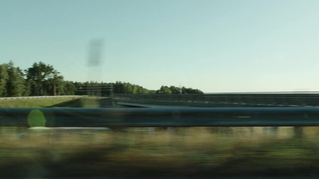Dynamic footage captures view from car window, showcasing blurred guardrail and verdant forest against clear summer sky, conveying movement and scenic route journey.