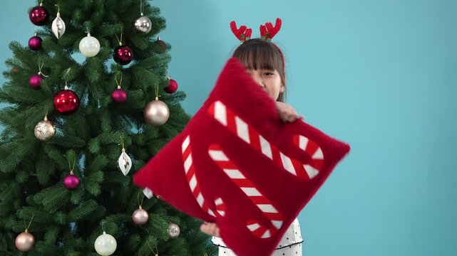 Happy young girl holding christmas pillow near tree