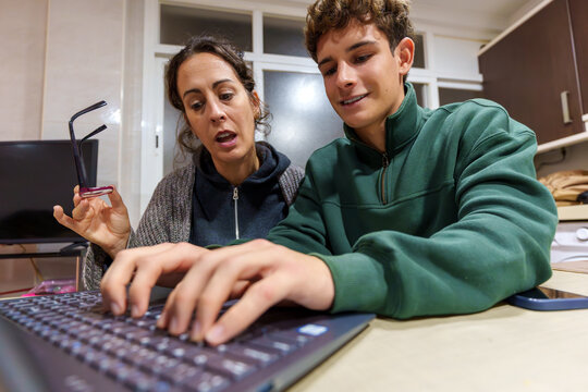 Teenage boy teaching mother digital literacy on laptop, sharing knowledge and bridging generations