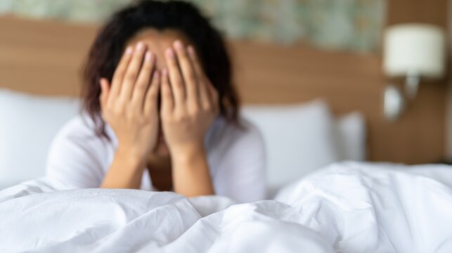 Person covers face while sitting on bed in hotel room during morning hours