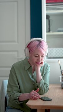 Relaxed positive mature woman reading blog feeds online on smartphone and listening music, tranquil smiling female in headphones enjoying favorite playlist, browsing social media online on cellphone