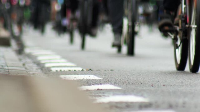 Ground level perspective of numerous cyclists moving forward on paved road, focus on dashed white line separating lanes, dynamic blur of wheels and legs in motion