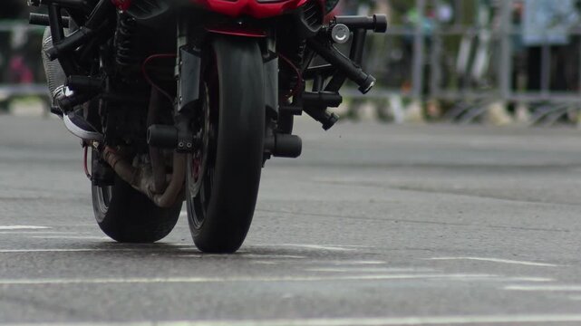 Close-up of red high-performance sportbike front wheel touching ground during a daring stunt. Rider demonstrates advanced control and precision. Exciting display of motorcycle handling on track.