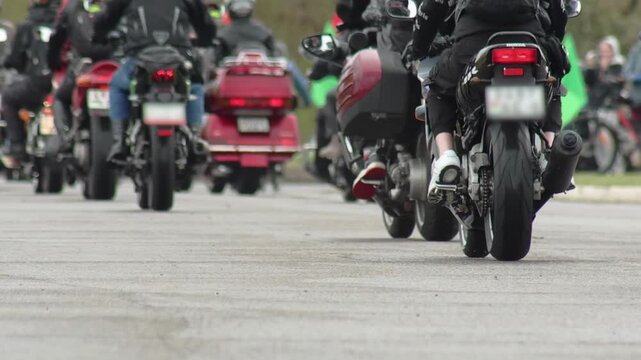 Close up low angle rear view of multiple motorcycles and riders during motorcycle rally, demonstrating movement of vehicle procession on paved surface, outdoor event activity
