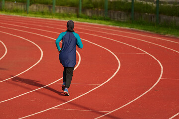 Fototapeta premium Female Runner In Hijab Jogging on Outdoor Red Track Lane for Fitness Training and Endurance