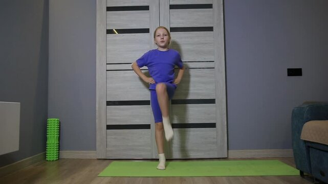 Full shot of young girl performing knee raise movement on green yoga mat, demonstrating physical exercise for fitness and development of children