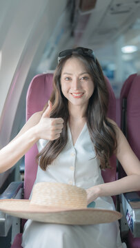 A happy Asian woman gives a thumbs-up while traveling on an airplane. The beautiful female passenger smiles and enjoys her plane ride on vacation.