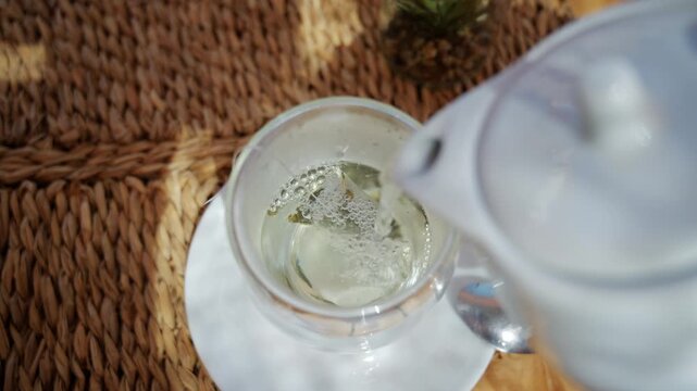 Close up of hot water being poured over a herbal tea bag in a glass cup
