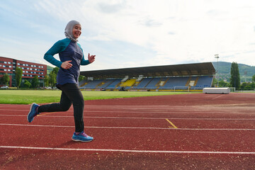 Fototapeta premium Smiling Muslim Woman Running on Track in Hijab Sportswear at Outdoor Stadium for Fitness