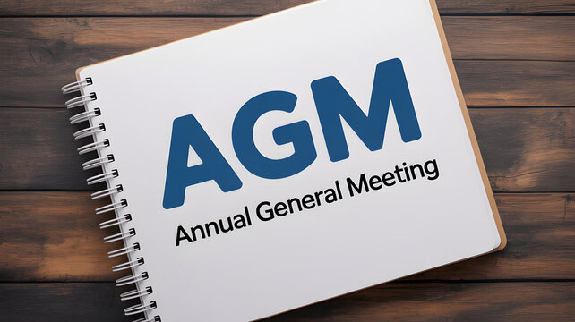 A spiral bound notebook with AGM Annual General Meeting text on a wooden table