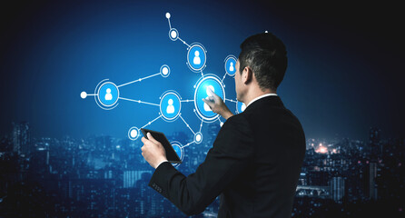 A businessman stands in a modern cityscape at night, engaging with a digital interface on his tablet, symbolizing connection and communication in a vibrant urban environment. Tessel © InfiniteFlow