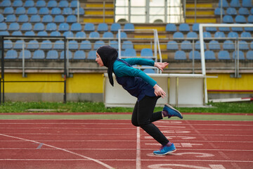 Obraz premium Female Athlete In Hijab Sprinting on Outdoor Track Stadium During Training Session