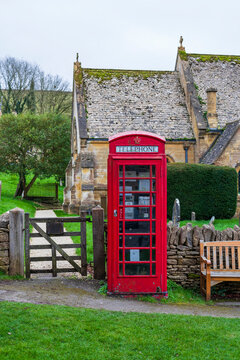 old english telephone box in front of a church made with oolitic limestone in Cotswolds, Uk