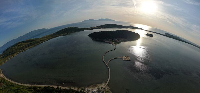 Aerial view of the Zvernec Monastery island and its long wooden bridge stretching across the Narta Lagoon under a bright sun Zvernec, Vlore County, Albania.