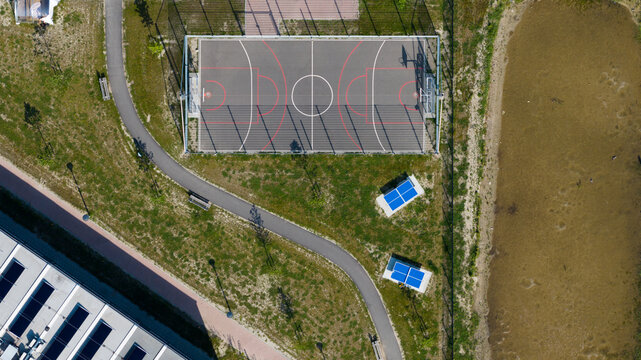 Aerial view of KaFra Zevenbergen featuring a basketball court, blue ping pong tables, and a winding path next to a building with solar panels in Zevenbergen, Noord-Brabant, Netherlands.