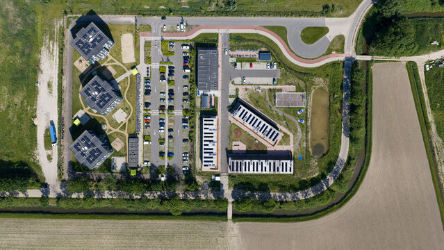 Aerial view of the KaFra Zevenbergen housing complex with modern buildings, solar panels, a parking lot, and surrounding green fields in Zevenbergen, Noord-Brabant, Netherlands.