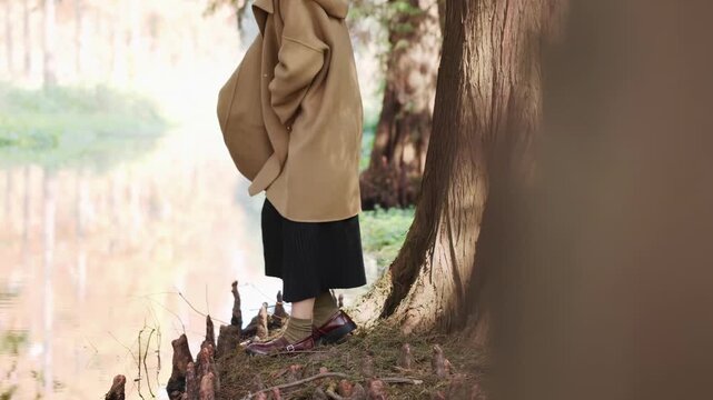Happy young tourist woman wearing winter hand tenderly reaches out to touch splashing water in nature landscape autumn park. Girl connect with natures serenity, tranquility in harmonious contemplation