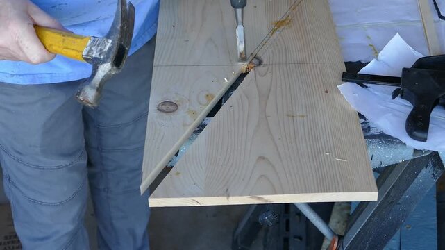 A woodworker uses a hand chisel to carefully cut and remove a small section of wood during a DIY woodworking project.