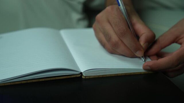 Hand holding and writing in pages of empty book on table, closeup