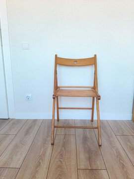 Wooden folding chair standing against empty white wall. Simple furniture piece for modern home interior. Minimalist design for study area, workspace, student room, generation z lifestyle.