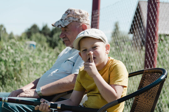 A grandfather and grandson in a yellow T-shirt enjoy fishing on a serene pond on their country property on a bright sunny day during a vacation, holiday or weekend out of town.