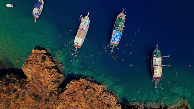 Aerial view of a rocky coastal cove with turquoise water, anchored boats and people swimming, ideal for summer travel, tourism, vacation, boat tours and Mediterranean lifestyle content.