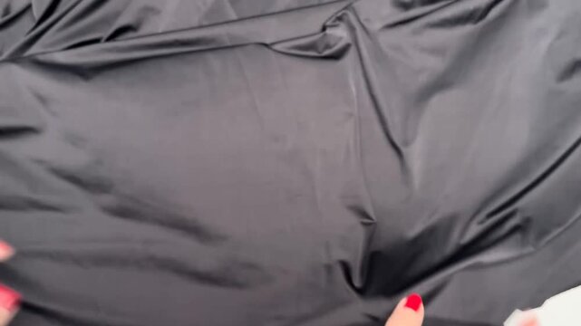 Hands stretch black micromoil textile revealing smooth texture high elasticity soft surface finish sheer quality and lightweight material composition suitable for apparel manufacturing.
