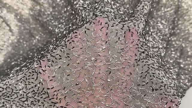 Hand stretches sheer silver sequin tube embellished stretch mesh fabric revealing shimmering metallic texture lightweight netting base soft drape and decorative evening apparel material