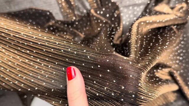 Close up of a sheer black and gold mesh textile featuring sparkling rhinestones and metallic stripes held by hands showcasing its stretch and glittery surface texture.