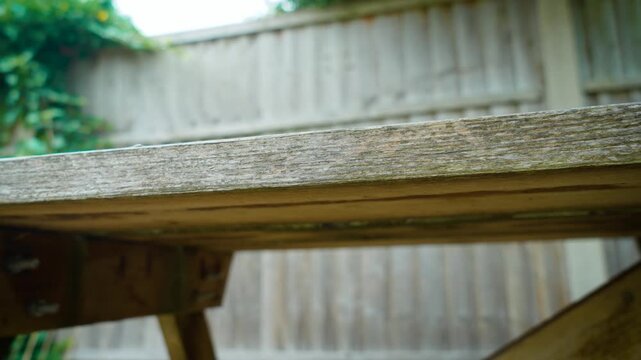 Wooden garden table standing in backyard patio beside privacy fence. Rustic outdoor furniture creating functional space for landscaping and garden organization. Residential backyard improvement