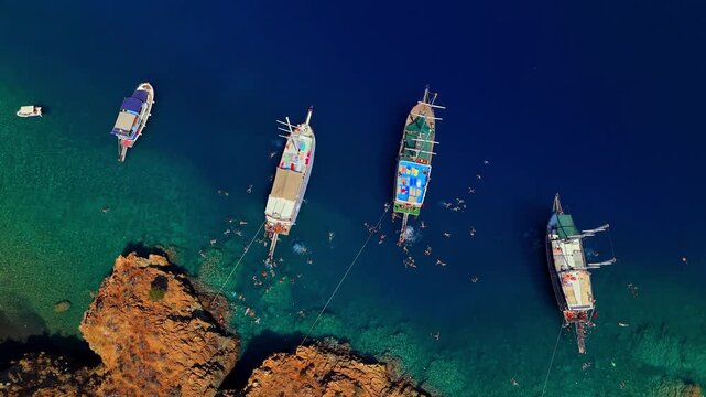 Aerial view of traditional gulet boats anchored near a rocky coastline in clear turquoise water, ideal for summer travel, coastal tourism, sailing, vacation and Mediterranean lifestyle content.