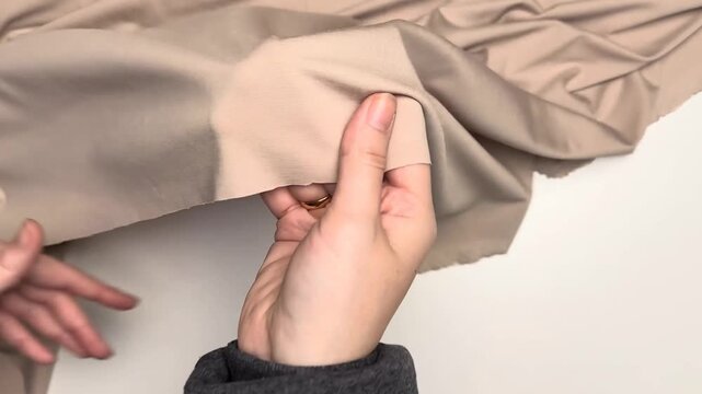 Beige knit fabric close up showing smooth matte texture elastic surface pattern and flowing material suitable for apparel garment and sewing projects
