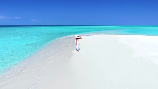 A beautiful woman in a white dress walks on a tropical paradise beach in the Maldives islands with fine sand and turquoise ocean