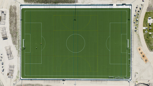 Aerial view of the green artificial turf football pitch at Sportpark Strandeiland with white markings and surrounding sandy areas in Amsterdam, North Holland, Netherlands.