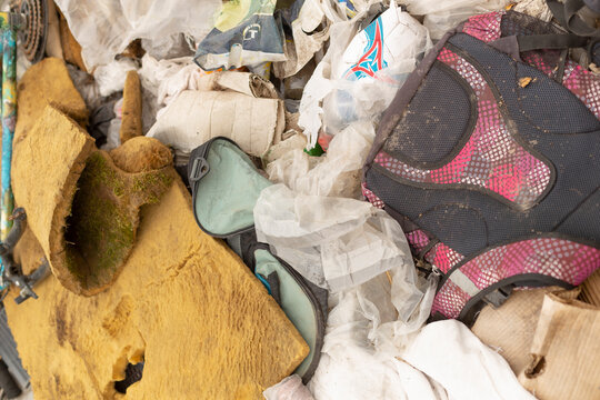 Close-up view of a worn pink and black backpack, shredded yellow car upholstery and assorted trash piled together in a landfill environment. The scene shows